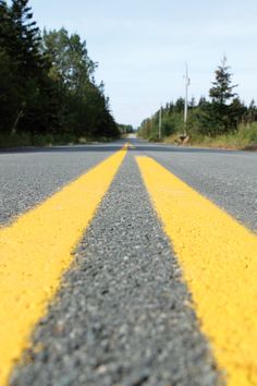 an empty street with yellow lines painted on the asphalt and trees in the background,