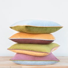 four pillows stacked on top of each other in different colors and sizes, all sitting on a wooden surface