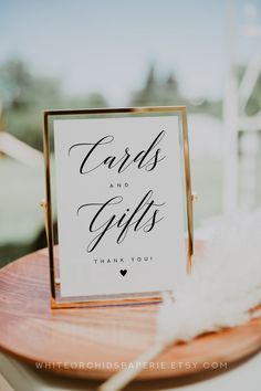 a sign that says cards and gifts is on top of a wooden table with feathers