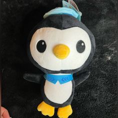 a small stuffed penguin with a blue ribbon around its neck and eyes, standing on a black surface