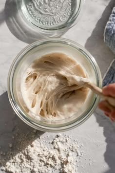 a person holding a spoon in a glass bowl filled with white powder next to another cup