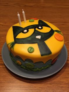 a birthday cake with yellow and green frosting on a wooden table next to two candles