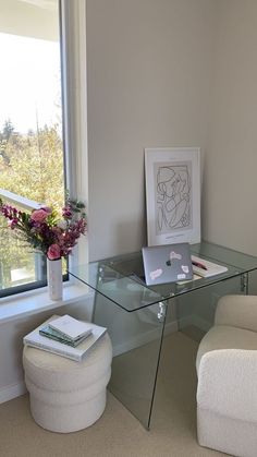 a glass desk with a laptop on it in front of a window next to a white chair