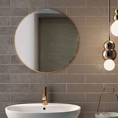 a white sink sitting under a round mirror next to a wall mounted faucet