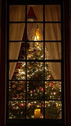 a lit christmas tree is seen through a window