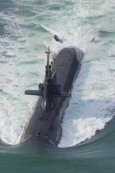 a submarine in the middle of some choppy water with people standing on it's side