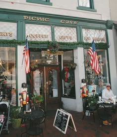 people are sitting at tables in front of a coffee shop with american flags hanging from the windows