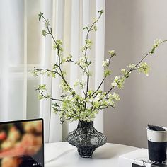 a vase filled with white flowers sitting on top of a table next to a laptop computer