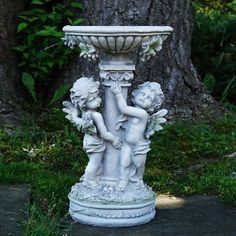 two cherubs are standing next to a water fountain on the ground in front of a tree