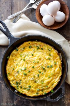 an omelet in a cast iron skillet on a wooden table next to eggs