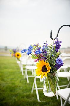 a row of white chairs sitting on top of a lush green field covered in lots of purple and yellow flowers