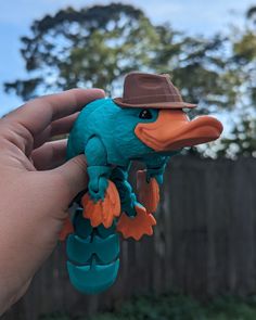 a hand holding a toy bird with a hat on it's head