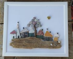 an art piece with rocks and houses on it in a white frame next to a wooden table