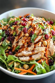 a salad with chicken, cranberries and nuts in a white bowl on a table