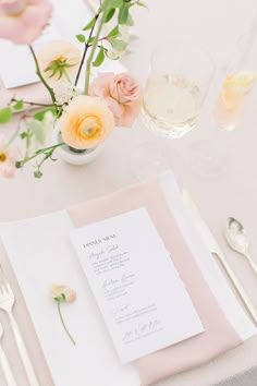 the table is set with pink and white flowers, silverware, and menu cards