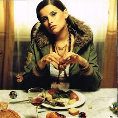 a woman sitting at a table with food and wine in front of her, making the shape of a heart