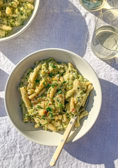 a white bowl filled with pasta next to two glasses of wine on top of a table