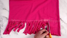 a person cutting fabric with scissors on a marble counter top next to a pink scarf