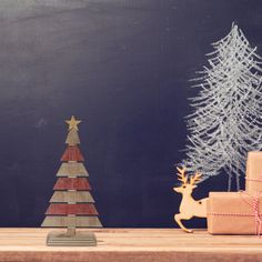 a small wooden christmas tree next to two wrapped presents on a table with chalkboard in the background