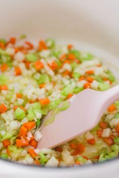 a white bowl filled with carrots, celery and onions next to a pink spatula