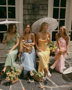 three women sitting on a bench with umbrellas over their heads and flowers in baskets