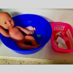 a baby doll sitting in a blue tub next to a pink basket