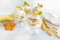 three desserts in small glasses on a table with gold utensils and bananas