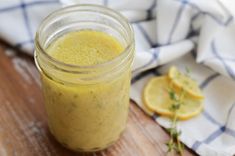 a jar filled with yellow liquid sitting on top of a wooden table next to sliced oranges