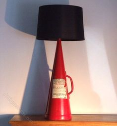 a red lamp sitting on top of a wooden table next to a black lampshade