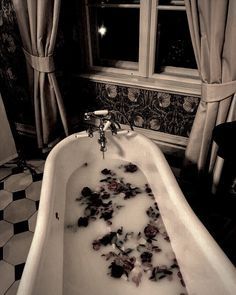 a bathtub filled with water next to a window covered in snow and roses on the floor