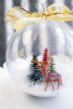 a glass ornament with two deer in the snow and a yellow bow on top