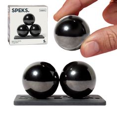 a hand is holding two black balls in front of a white box and an object