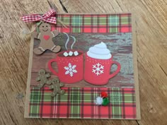 a christmas card with gingerbreads and hot chocolate in red mugs on a plaid tablecloth