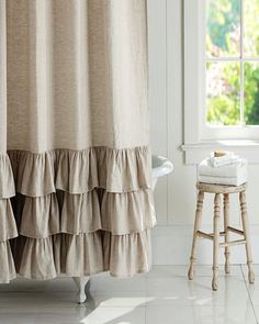 a white bath tub sitting under a window next to a wooden stool with towels on it