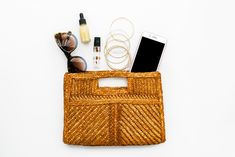 the contents of a wicker purse laid out on a white surface with sunglasses, cell phone and other items