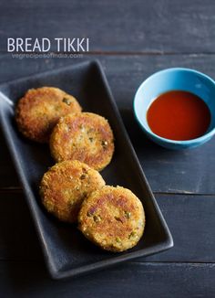 four crab cakes on a black plate next to a cup of tea