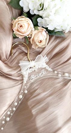 a bridal hanger with flowers and pearls on it next to a satin fabric