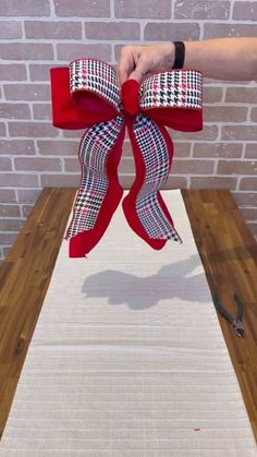 a person is holding a red bow on top of a white tablecloth with a brick wall in the background