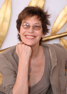 a woman with glasses sitting in front of a gold wall and smiling at the camera