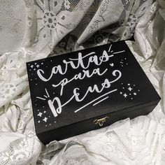 a black box with white writing sitting on top of a bed covered in laces