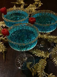 three martini glasses with raspberries sit on a table next to gold foil foliage