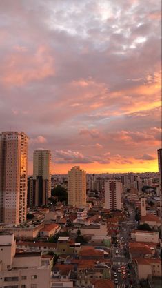 the sun is setting over a city with tall buildings in the foreground and clouds in the background