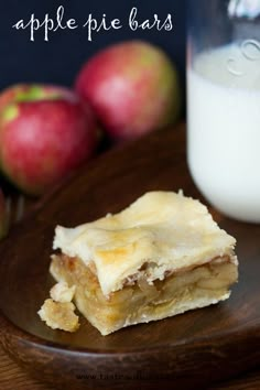 apple pie bars on a wooden plate next to a glass of milk and some apples