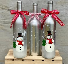 three stainless steel wine bottles with snowmen painted on them and red ribbon tied around the top