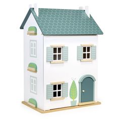 a white doll house with blue windows and green shutters on the front, sitting on top of a wooden table