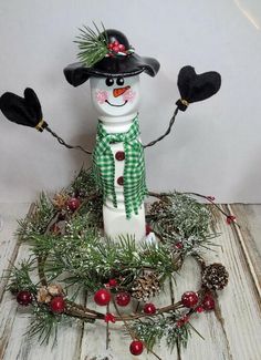 a snowman is standing in front of some pine cones and berries on the table