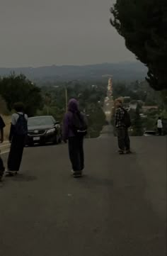 three skateboarders are riding down the street in front of some cars and trees