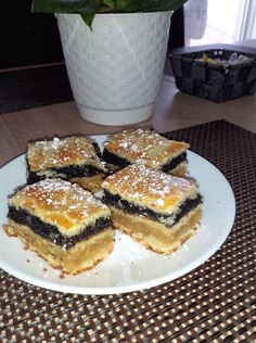 four pieces of dessert sitting on a white plate next to a potted plant in the background