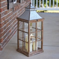 a lantern with three candles in it sitting on the ground next to a brick wall