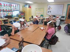 a group of children sitting at a table in a classroom with paper hats on their heads